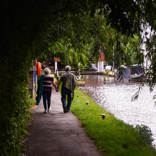 senior couple walking along lake embankment holding hands