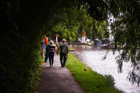 senior couple walking along lake embankment holding hands