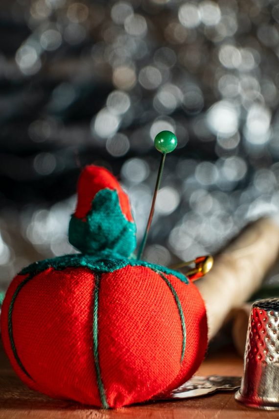 close up shot of a red pincushion beside a thimble