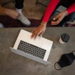 unrecognizable black colleagues browsing laptop at table with face mask