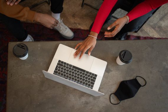 unrecognizable black colleagues browsing laptop at table with face mask